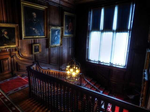 A staircase in a dark room with a chandelier and paintings on the wall.