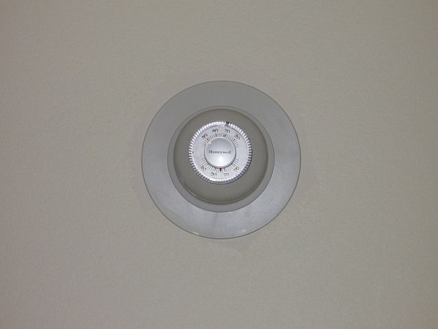 A white thermostat is hanging on a white wall.