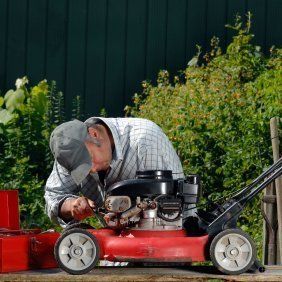 A man is fixing a lawn mower on a bench.