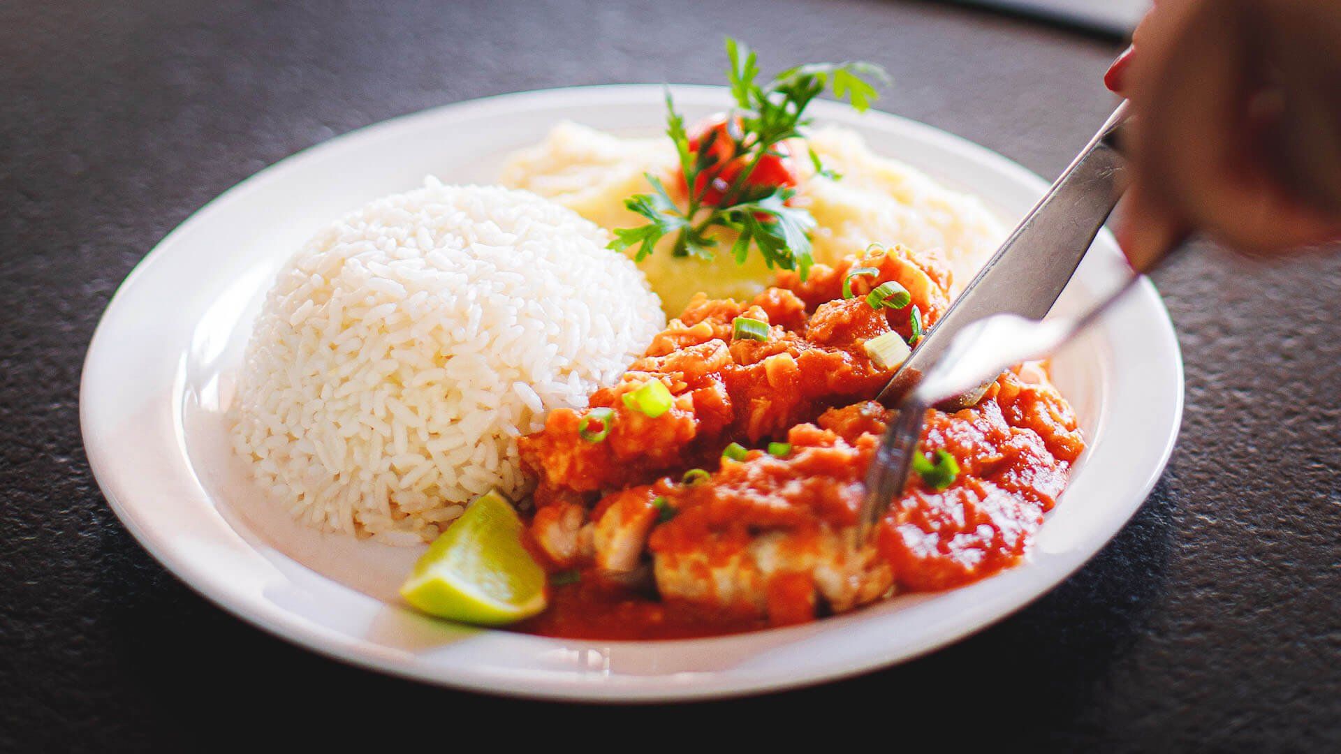 Uma pessoa está cortando um prato de comida com arroz e molho.