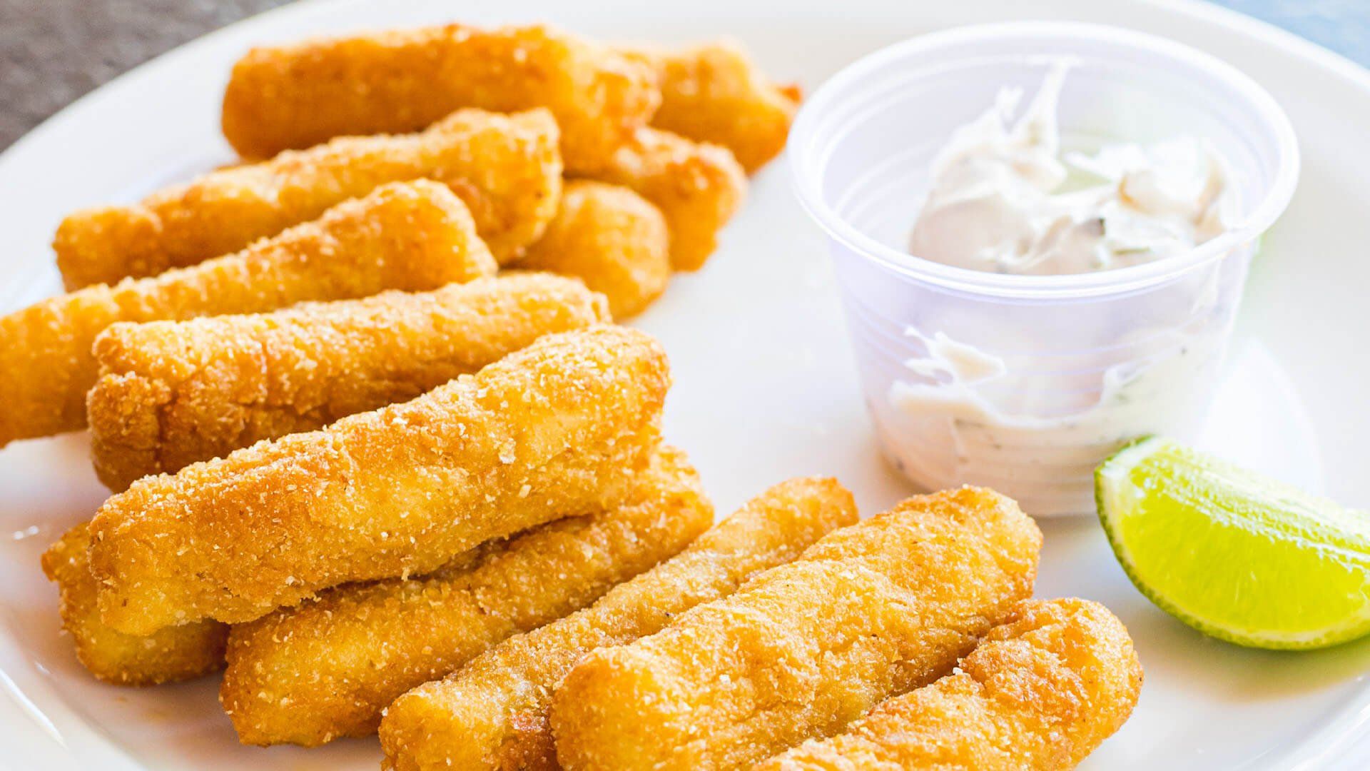 Um prato branco coberto com palitos de peixe fritos e um molho para mergulhar.