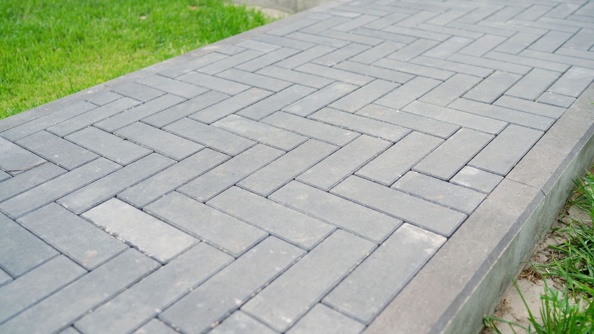 Gray brick sidewalk with a herringbone pattern beside green grass