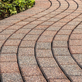 Curved red and gray brick walkway leading through a garden with green plants along the edge