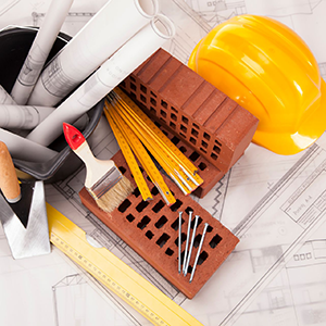 Construction tools, rolled blueprints, bricks, ruler, and yellow hard hat on architectural plans
