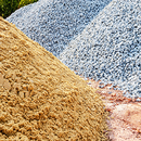 Piles of sand, gravel, and crushed stone in tan, blue-gray, and pink hues