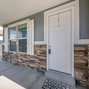 Front entrance with white door, window, stone accent wall, and welcome mat on a concrete porch.