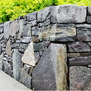 Gray stone retaining wall beside a sidewalk, topped with bright green foliage