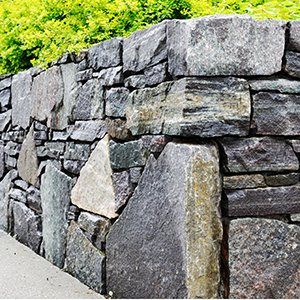 Gray stone retaining wall beside a sidewalk, topped with bright green foliage
