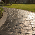 Curved stone garden walkway beside green lawn, wet and reflecting sunlight