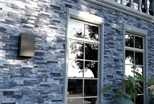 Stone exterior wall with two windows and a wall-mounted light fixture, partially framed by greenery