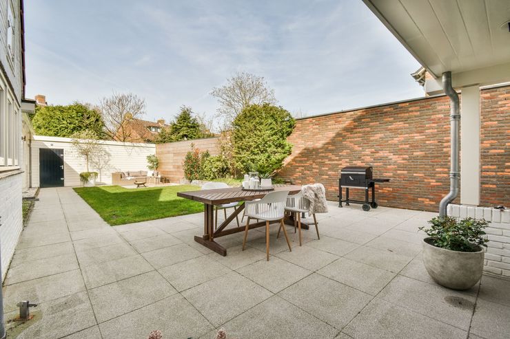 Spacious brick patio with outdoor dining table, chairs, grill, potted plant, and lawn by a garden wall.