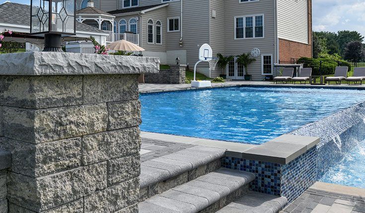 Backyard swimming pool with stone coping, steps, and a residential apartment building in the background