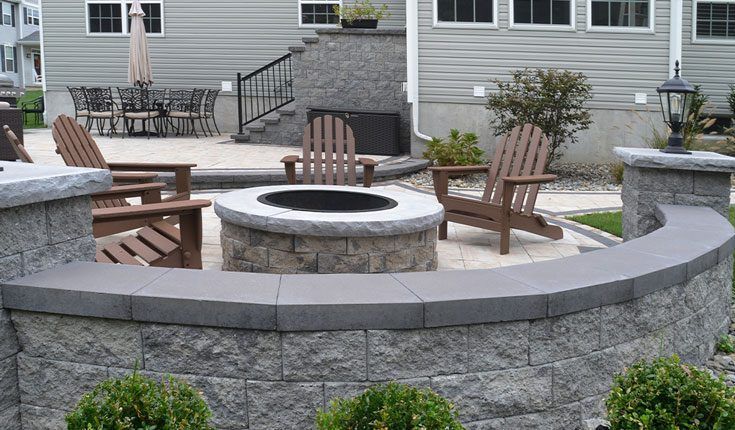 Stone patio with circular fire pit and wooden chairs in a backyard seating area