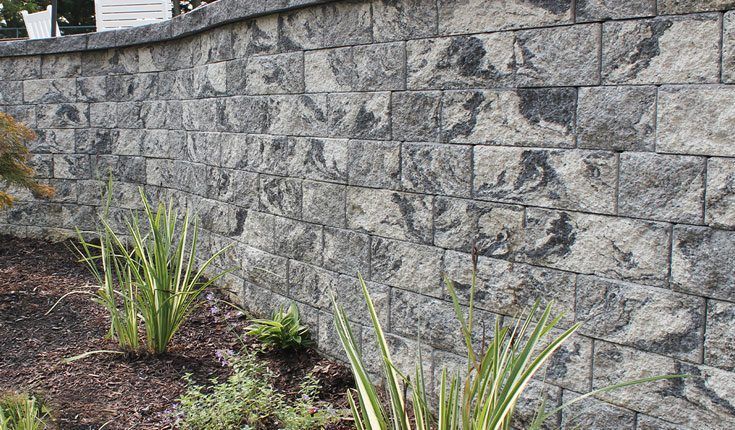 Gray stone retaining wall with small green plants and mulch in the foreground