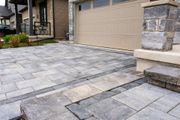 Stone-paved driveway leading to a beige garage door and front entrance with stone pillars