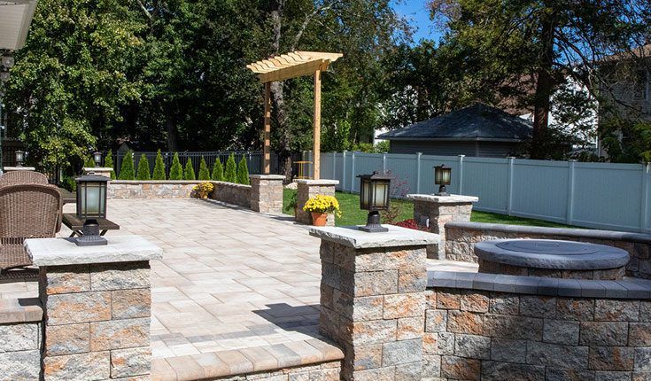 Stone patio with lanterns, planter boxes, and a pergola in a sunlit backyard garden