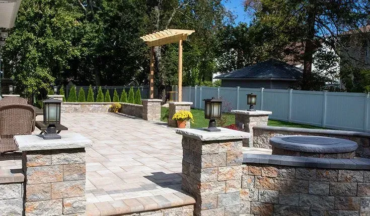 Stone patio with lanterns, planter boxes, and a pergola in a sunlit backyard garden