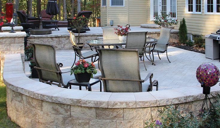 Outdoor stone patio with table and chairs, potted flowers, and house exterior in the background