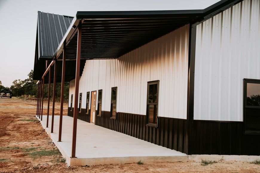Metal building with a black roof and trim, and a white exterior. A covered porch runs along the side.