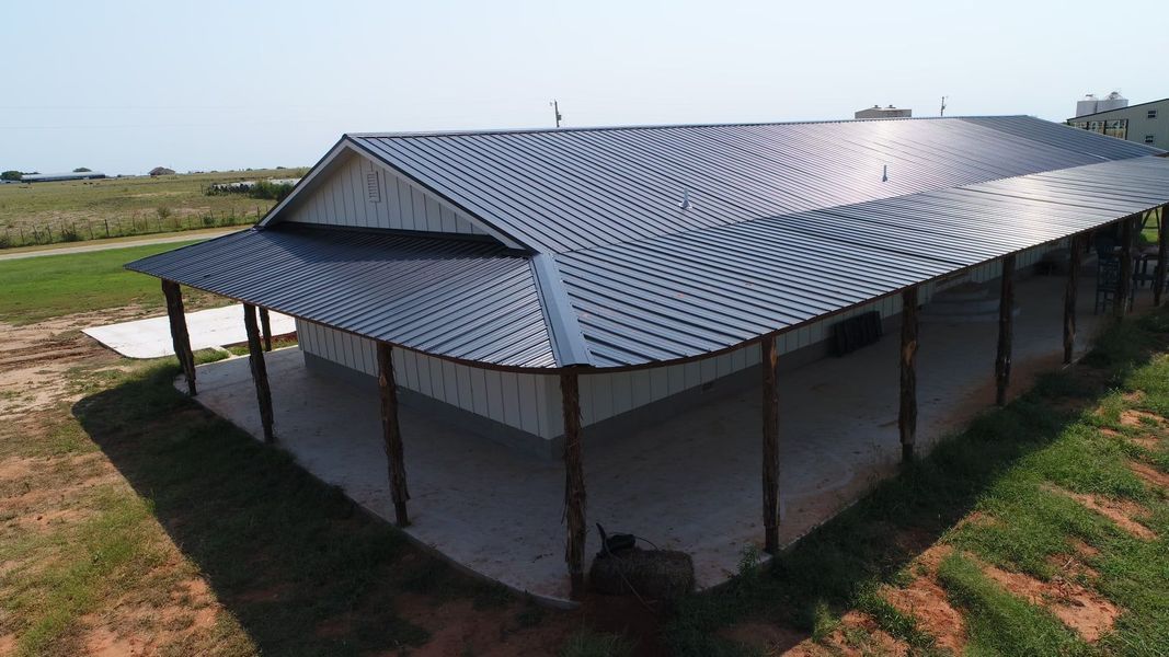 Metal-roofed building with porch. Gray metal roof, white siding, and porch supported by wooden posts in a grassy area.