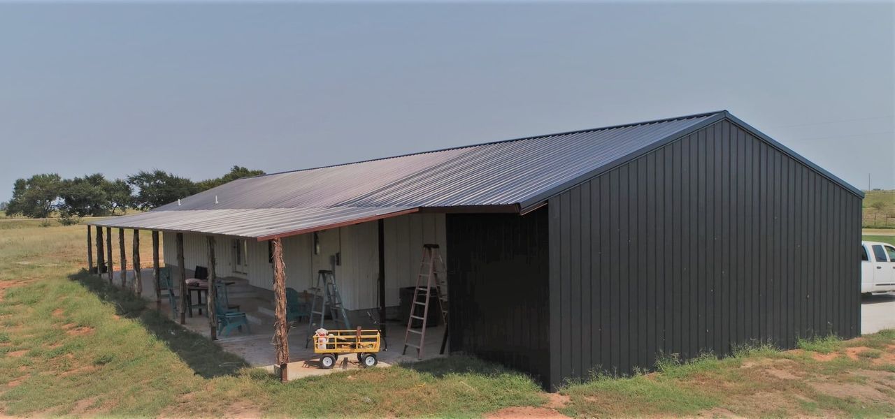 A large, dark gray metal building with a covered porch in a grassy field.