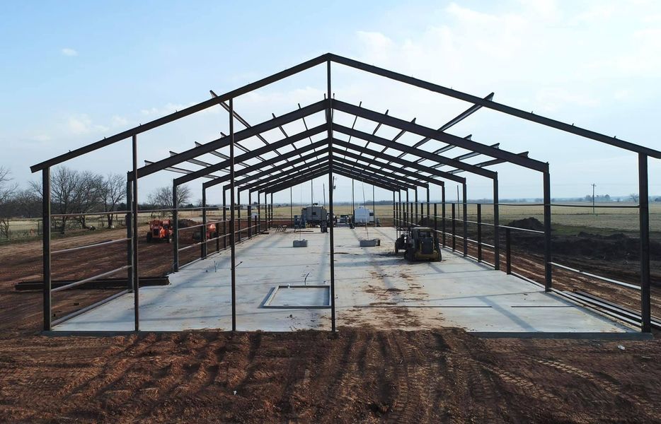 Steel frame barn under construction, on a concrete slab, set in a field.