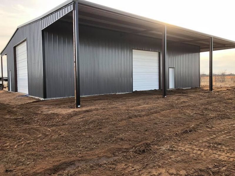 Dark gray metal barn with white garage doors and an attached awning.