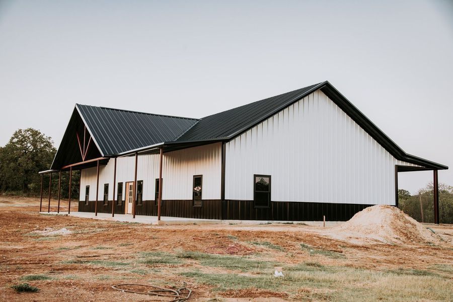White barn with black roof and trim on brown dirt, exterior view.