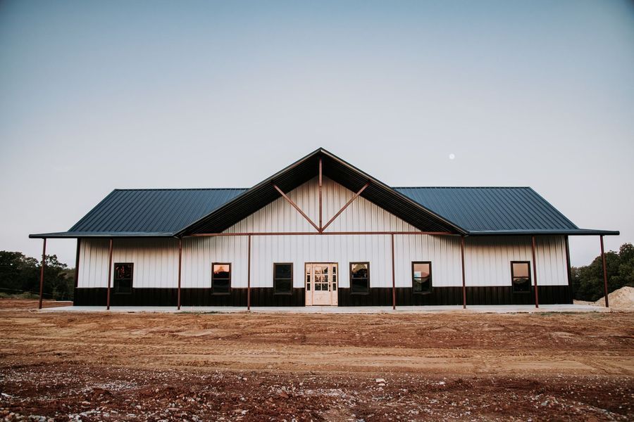 White barn with black accents, blue roof, open front door, and windows.