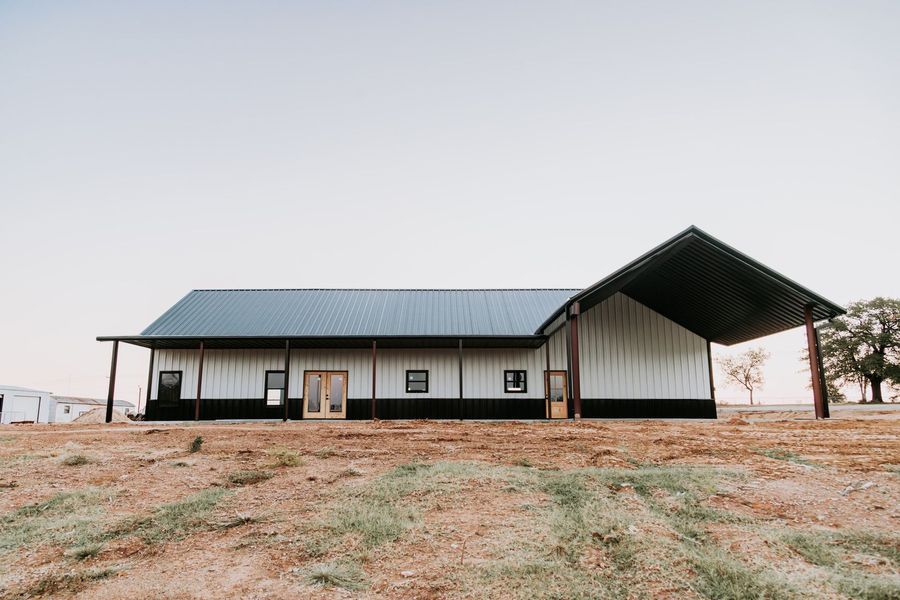 Barn-style building with black and white exterior, blue roof, and covered porch on a hilltop against a clear sky.