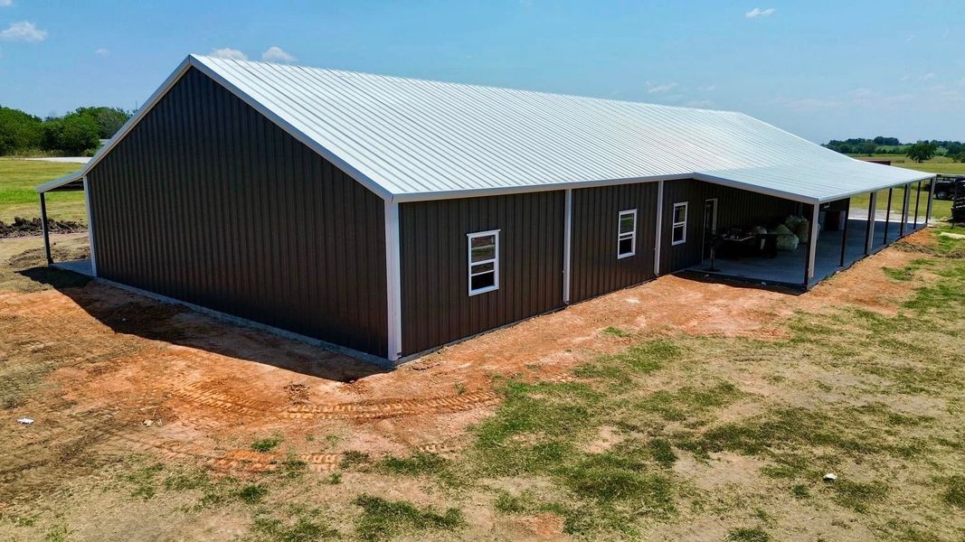 Brown and silver metal building with a covered porch on a dirt lot under a blue sky.