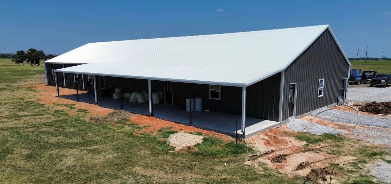 Large gray metal building with a white roof on a grassy field.