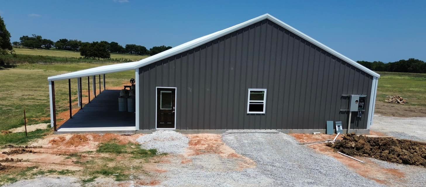 Gray metal building with a white roof and a covered porch on a gravel driveway.