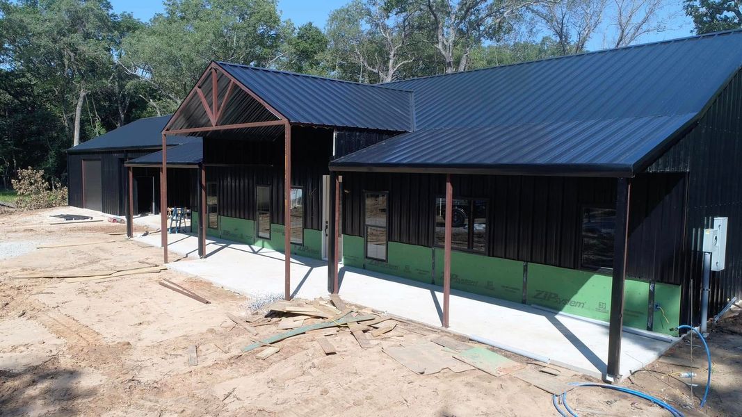 Black metal-clad building with a dark roof and concrete foundation under construction.