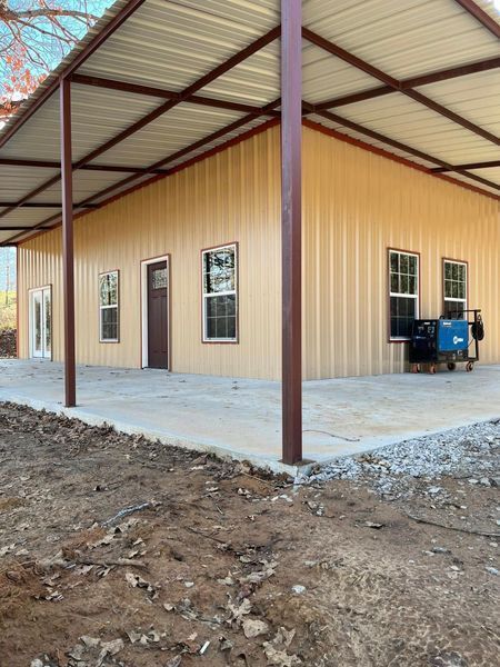 Tan metal building with brown trim, covered porch, concrete pad, and dirt ground.