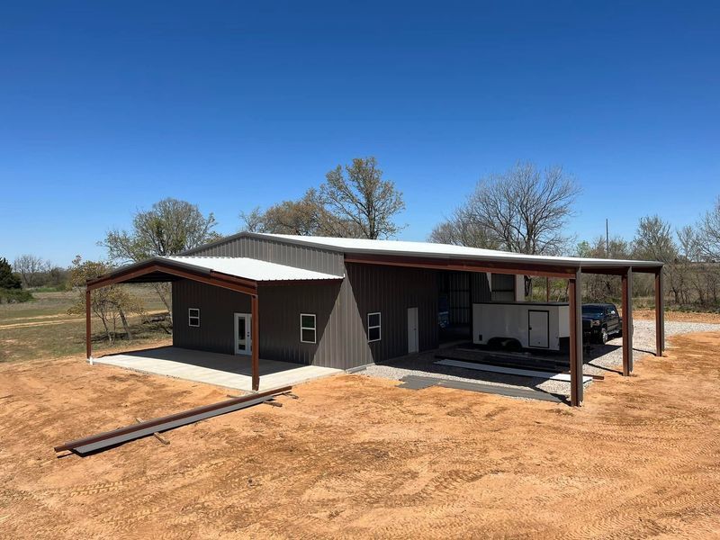 Brown metal building with attached carport under a blue sky.