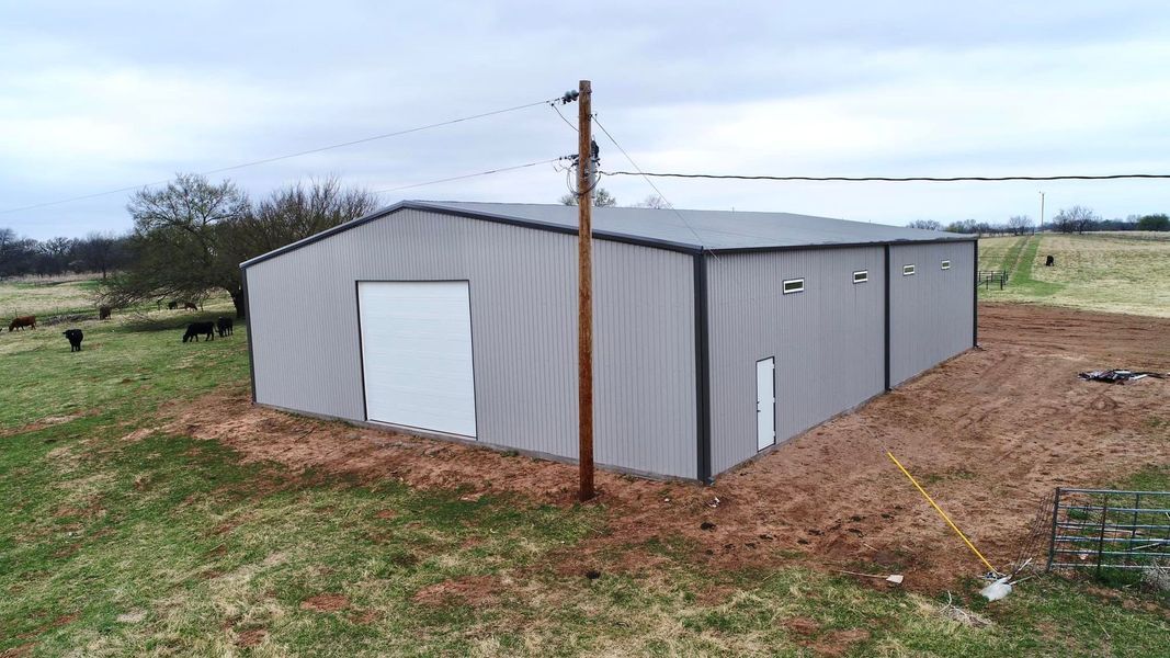 Gray metal barn with large doors and windows on a grassy field with utility pole.