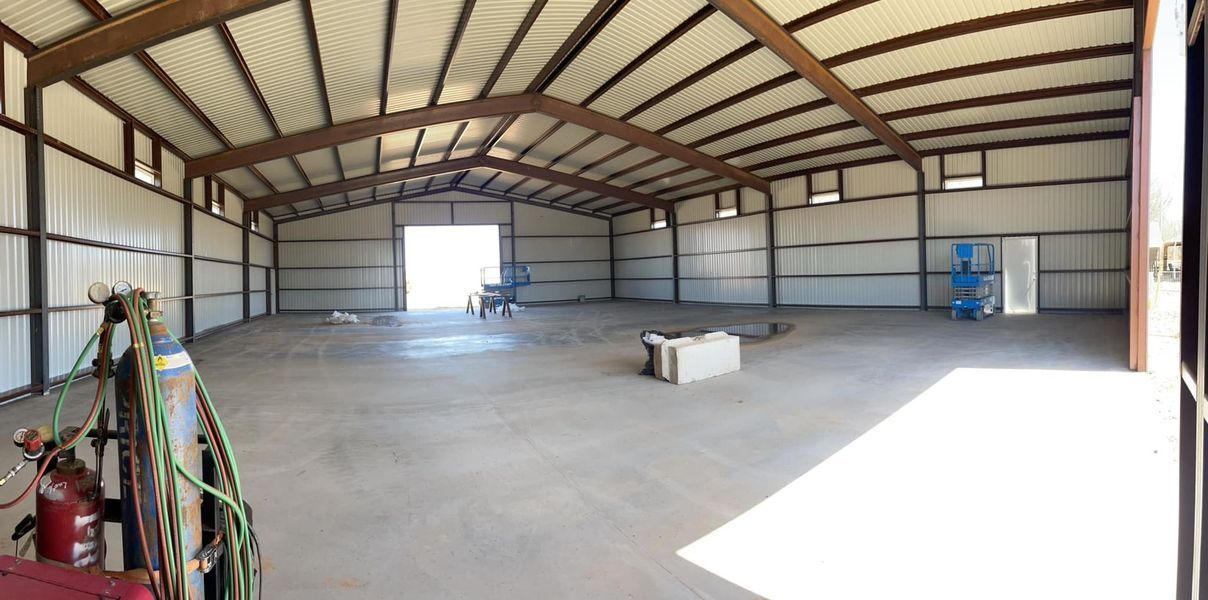 Interior of an empty warehouse with a large open doorway, metal framework, and concrete floor.