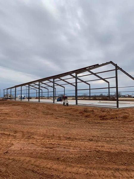 Steel frame of a large building under construction on a concrete foundation, cloudy sky.