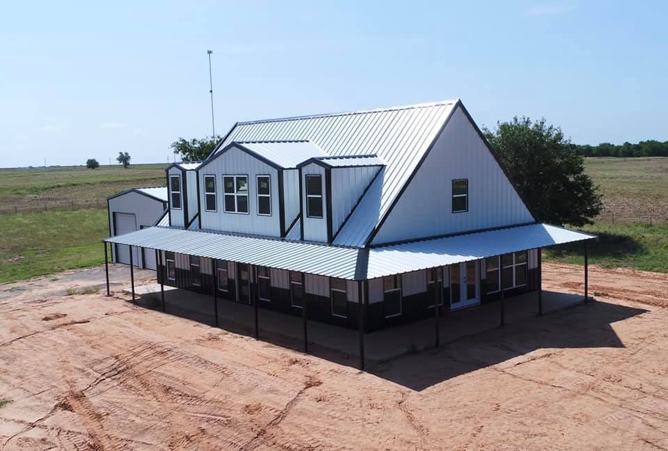 White house with a metal roof and large porch on a rural property.