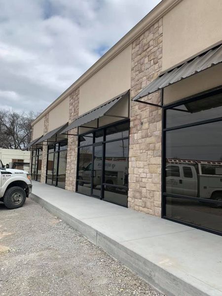 Commercial building exterior with stone and tan facade, large windows, awnings, and a concrete walkway.
