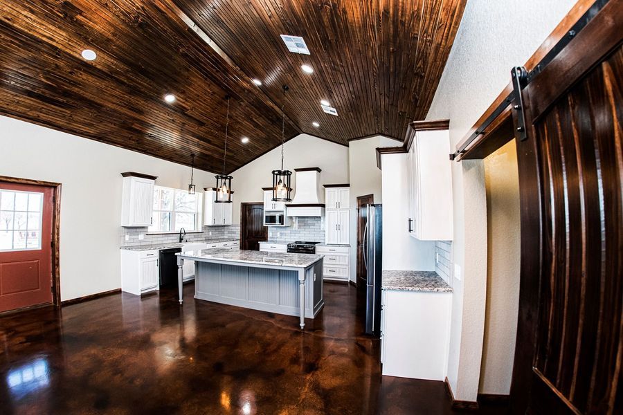 Kitchen with wooden ceiling and floor, white cabinets, gray island, and brown sliding door.