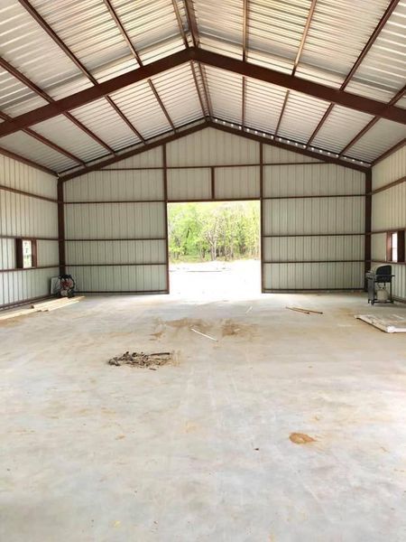 Interior of a large metal building with a concrete floor and open doorway to the outside.