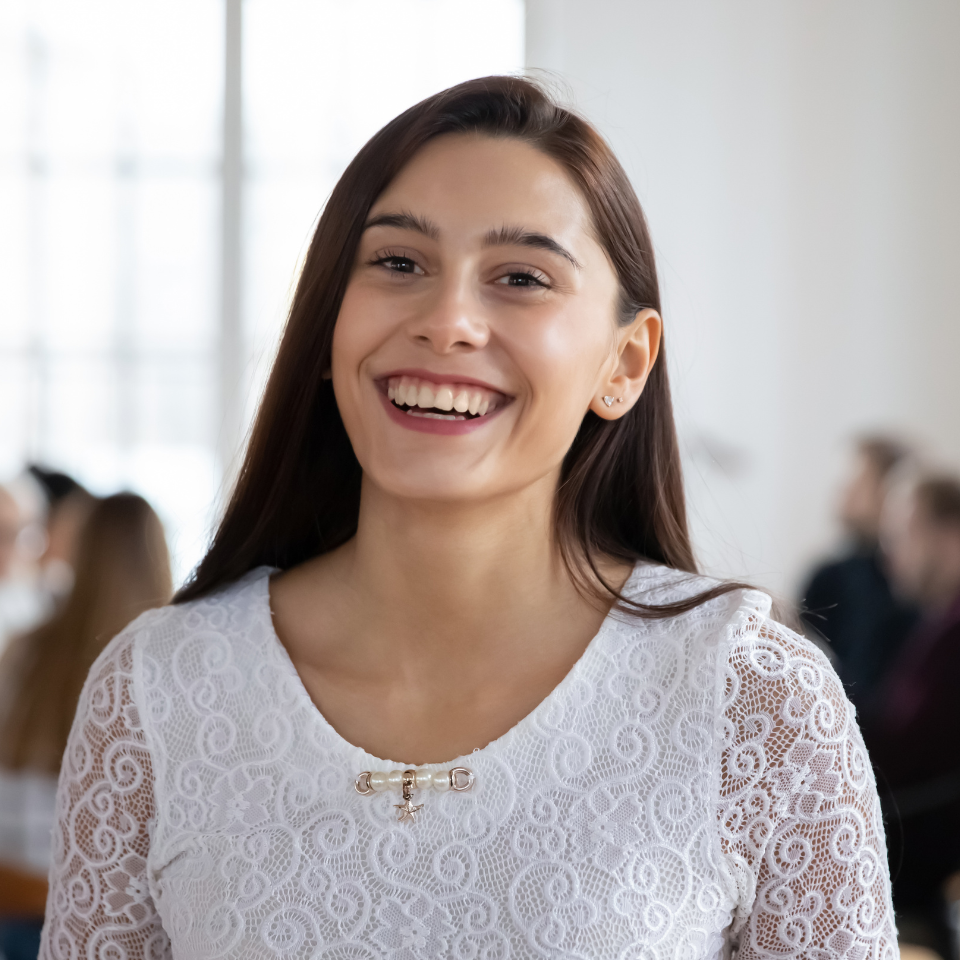 A woman in a white lace top is smiling and looking at the camera.