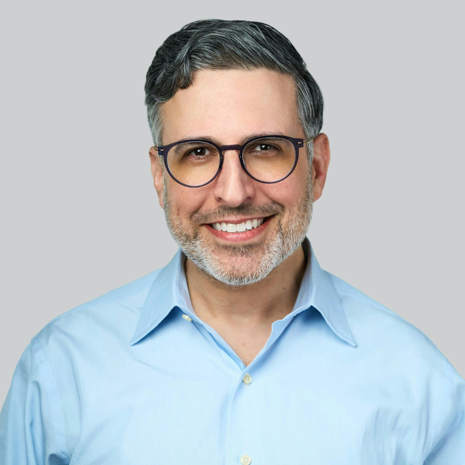 A man with glasses and a beard is smiling for the camera.