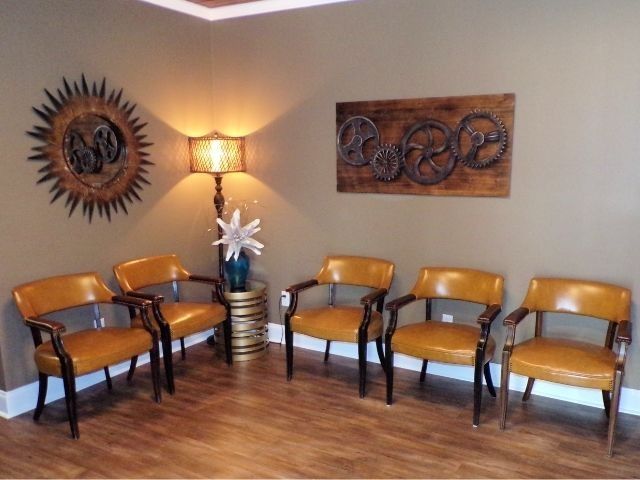 Waiting room with six tan chairs, a floor lamp, and wall art on wood flooring.