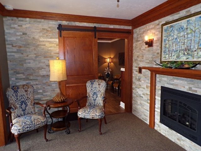Cozy living room with stone fireplace, two patterned chairs, side table, lamp, and wooden sliding door