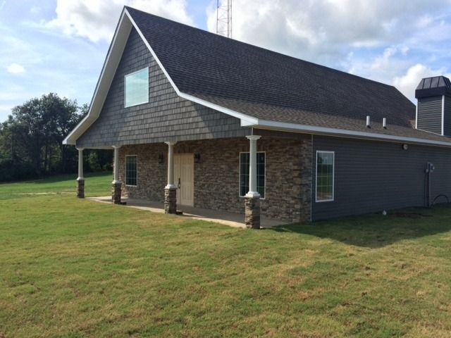 Brick house with a dark roof and white trim on a grassy lawn under a partly cloudy sky