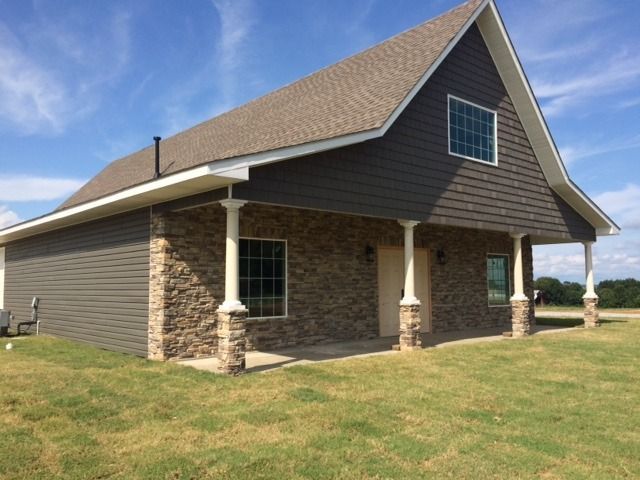 Stone-and-siding house with a brown roof and covered porch on a grassy lot under a blue sky