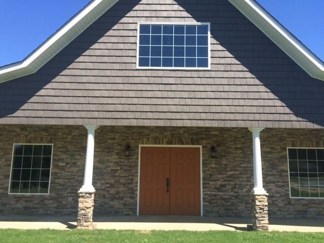 Front view of a stone house with brown double doors, white columns, and a gabled roof with a central window
